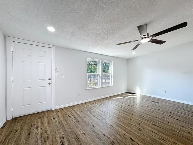 an empty room with wooden floor ceiling fan and windows
