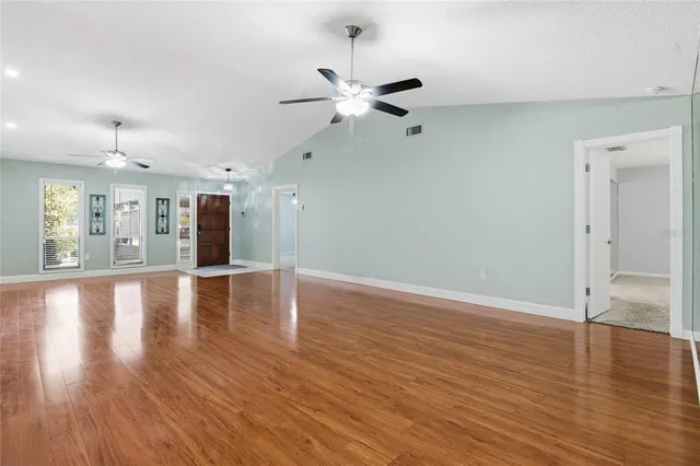a view of an empty room with wooden floor and a ceiling fan