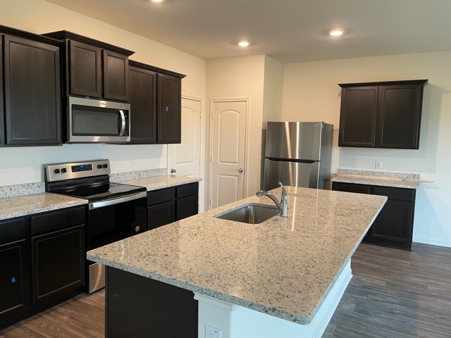 18812 Speculator Lane Elgin, TX 78621 - Photo 7 of 24 Kitchen featuring appliances with stainless steel finishes, light stone counters, dark wood-style floors, an island with sink, and recessed lighting