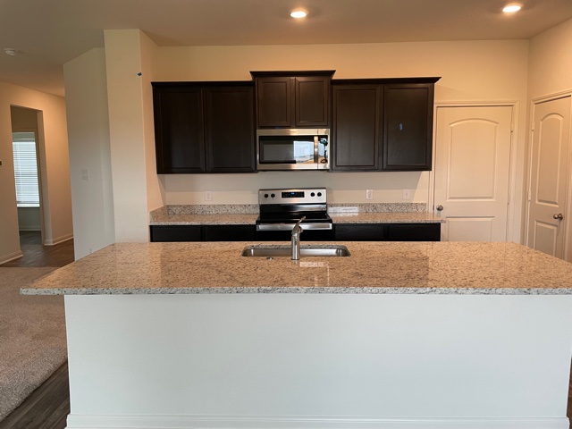 18812 Speculator Lane Elgin, TX 78621 - Photo 8 of 24 Kitchen featuring appliances with stainless steel finishes, a center island with sink, light stone countertops, recessed lighting, and dark brown cabinets