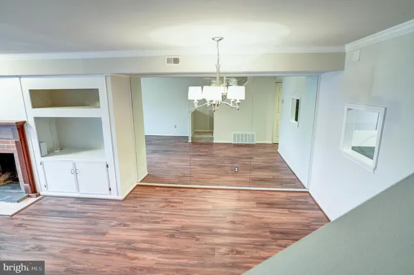 a view of an empty room with wooden floor and kitchen view