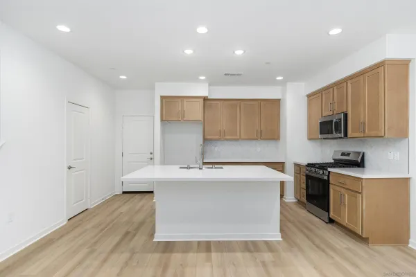 a large kitchen with stainless steel appliances granite countertop a stove top oven a sink dishwasher and white cabinets with wooden floor