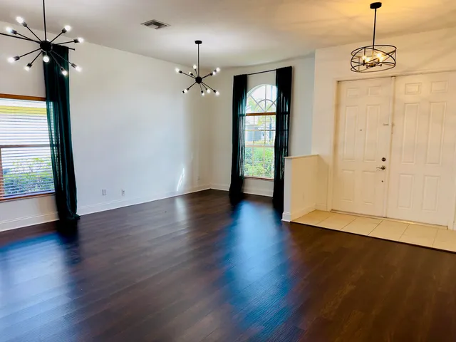 an empty room with wooden floor chandelier and windows