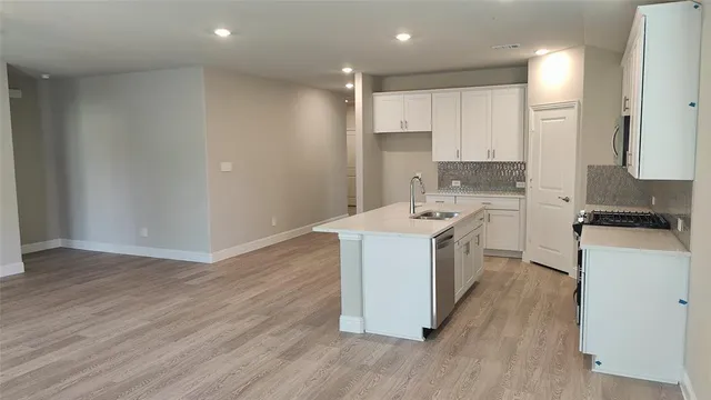 a kitchen with stainless steel appliances a microwave a stove a sink and white cabinets with wooden floor