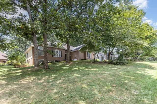 a tall tree in middle of green field in front of house