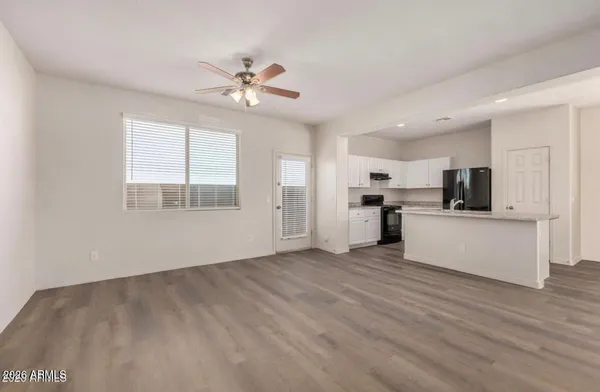 a view of an empty room with kitchen view and wooden floor
