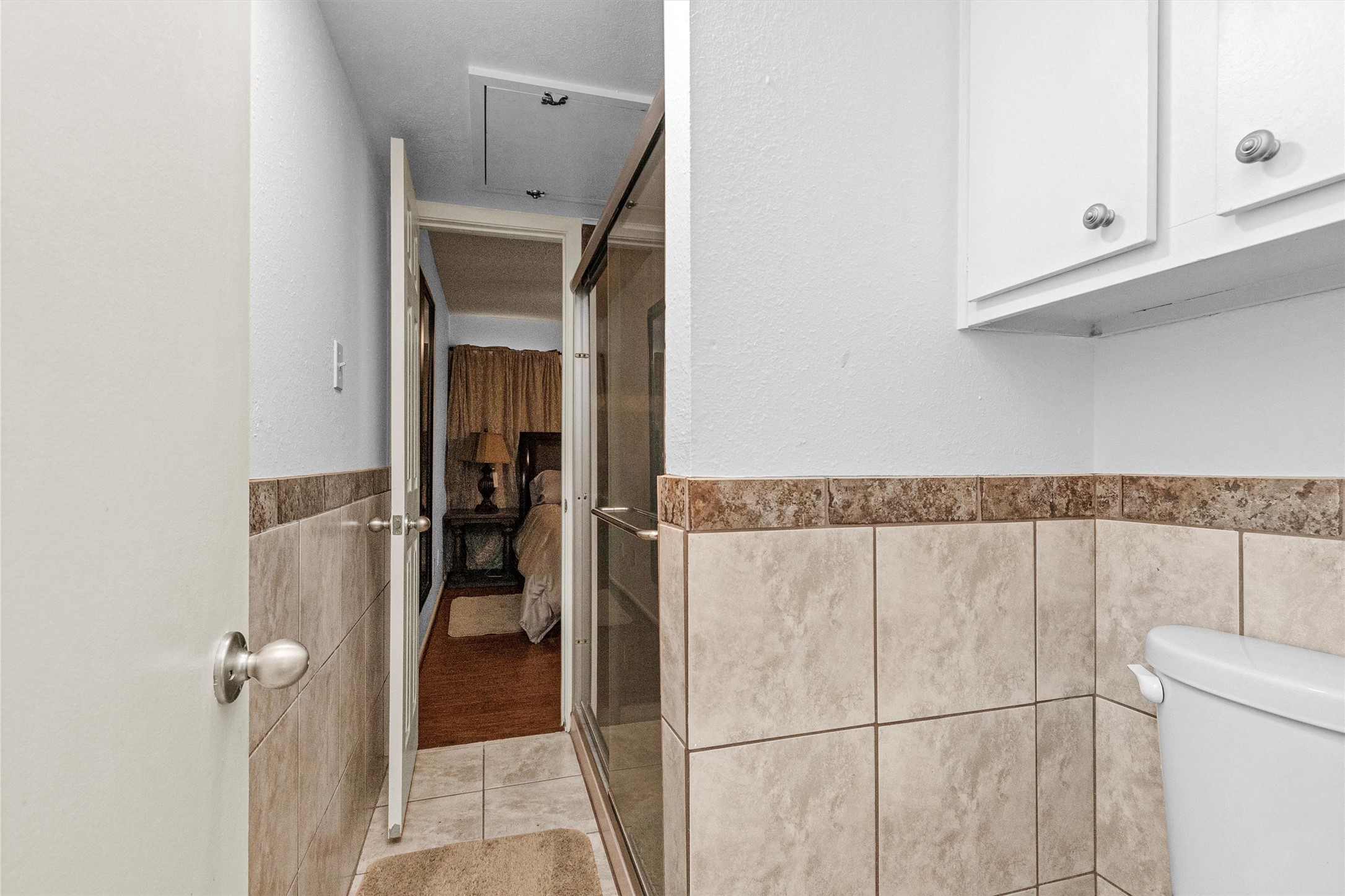 12900 Walden Road, Unit D 411 Montgomery, TX 77356 - Photo 10 of 18 This inviting bathroom features stylish tiled walls, a convenient shower enclosure, and ample storage with upper cabinetry, seamlessly connecting to a cozy bedroom through an open doorway.