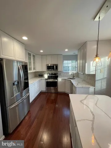 a kitchen with stainless steel appliances granite countertop a refrigerator a sink dishwasher a stove and white countertops with wooden floor