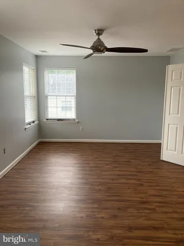 an empty room with wooden floor fan and windows