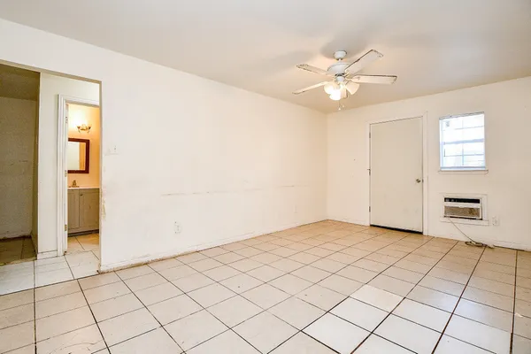 an empty room with a chandelier fan and kitchen view