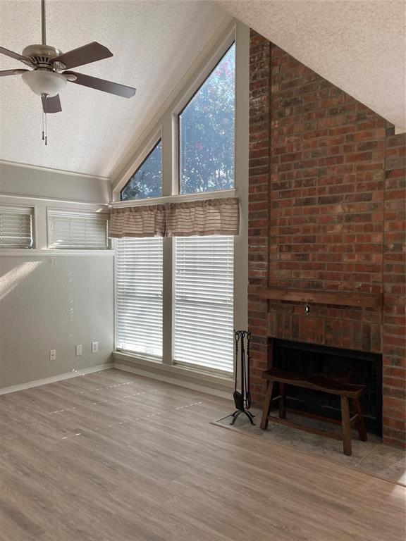 18240 Midway Road, Unit 905 Dallas, TX 75287 - Photo 3 of 15 Unfurnished living room featuring a high textured ceiling, a brick fireplace, a ceiling fan, light wood-style flooring, and plenty of natural light