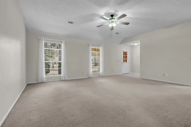 an empty room with chandelier fan and windows