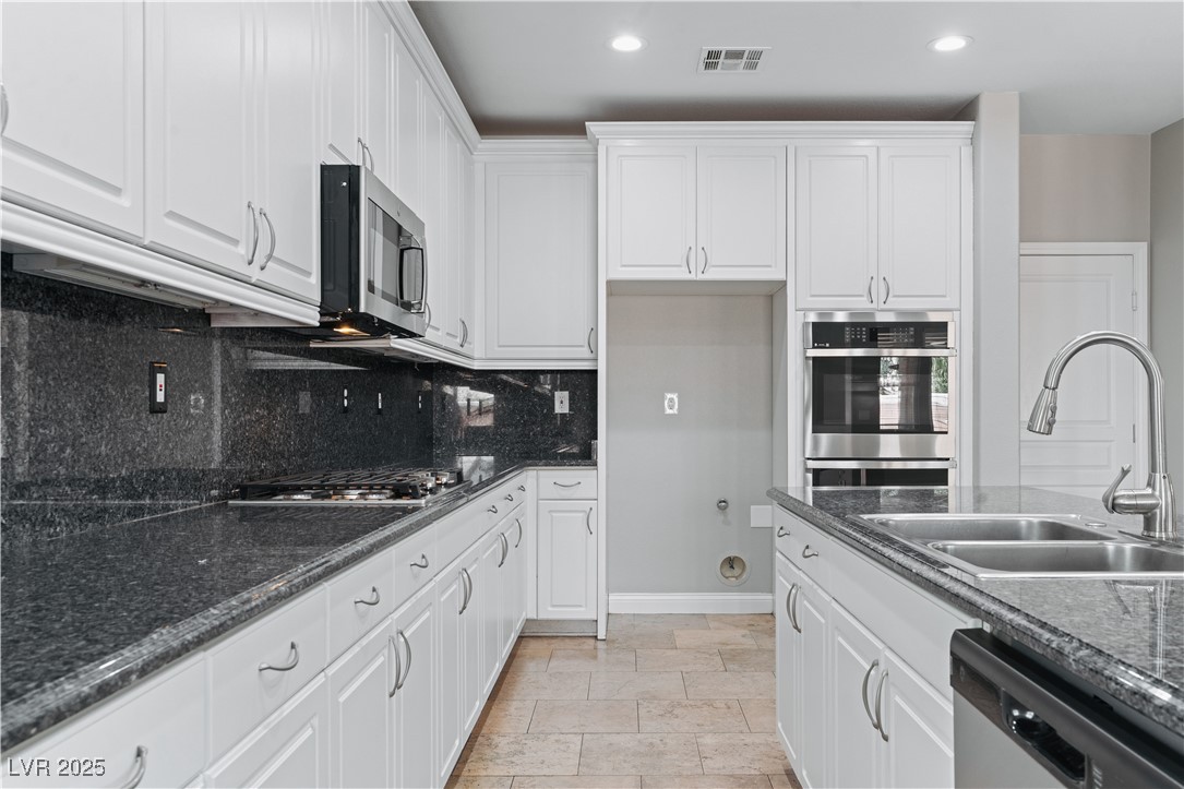 312 Pocono Ranch Avenue North Las Vegas, NV 89031 - Photo 5 of 34 Kitchen with tasteful backsplash, appliances with stainless steel finishes, white cabinets, a sink, and visible vents