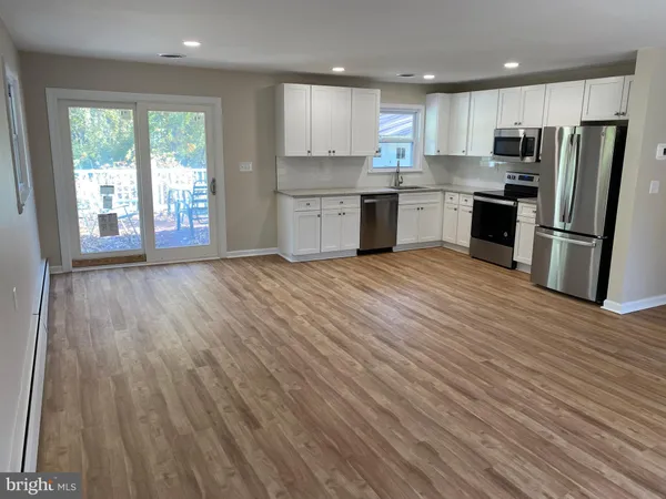 a kitchen with stainless steel appliances granite countertop a refrigerator a sink dishwasher a stove and white countertops with wooden floor