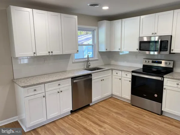 a kitchen with stainless steel appliances granite countertop white cabinets a sink a stove a refrigerator and microwave with wooden floor