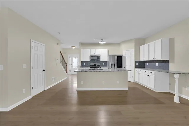 a large kitchen with stainless steel appliances granite countertop a stove a sink a refrigerator and white cabinets with wooden floor