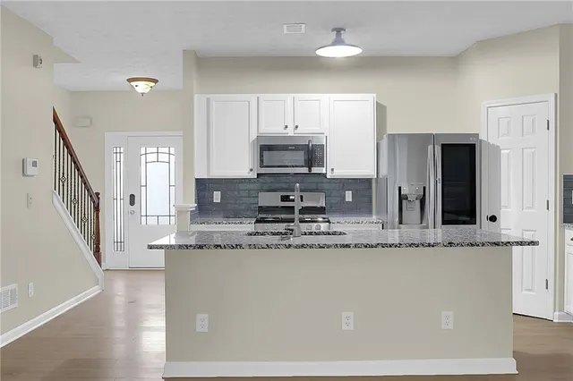 a large kitchen with granite countertop a stove a sink a refrigerator a microwave oven with white cabinets and wooden floor