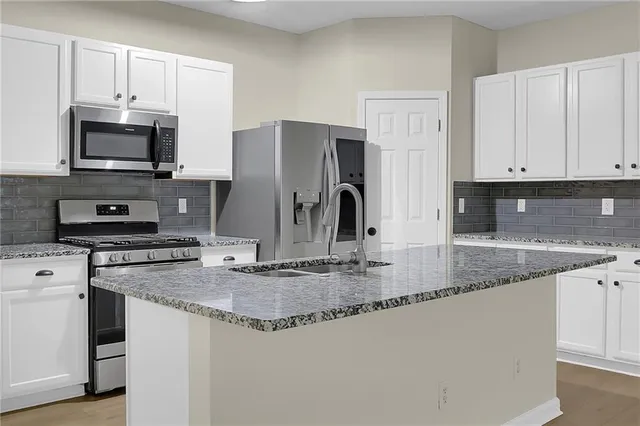 a kitchen with kitchen island granite countertop a sink a stove a refrigerator and white cabinets