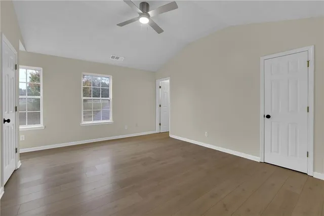 an empty room with wooden floor closet and windows