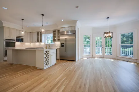 a kitchen with stainless steel appliances granite countertop a refrigerator a oven a island and white cabinets with wooden floors