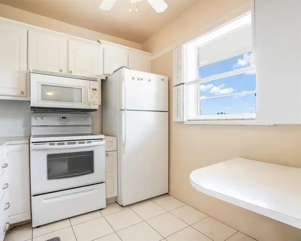 a white refrigerator freezer and a stove sitting inside of a kitchen with granite countertop white cabinets
