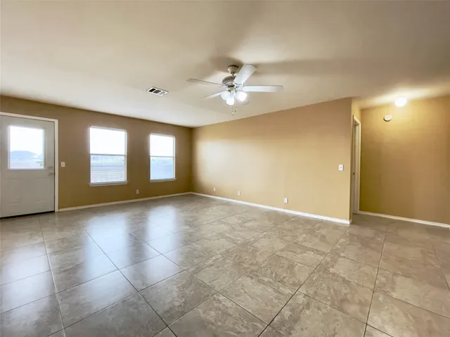 an empty room with chandelier fan and windows