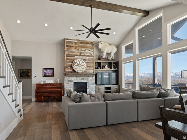 641 West 500 South Midway, UT 84049 - Photo 9 of 52 Vaulted ceiling great room with wood-finish flooring, a stone and wood fireplace, an exposed wood beam, large picture windows, and a black ceiling fan