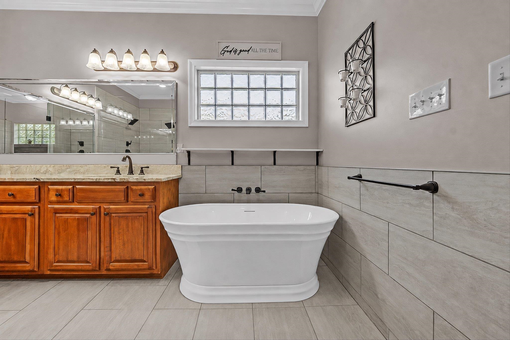 7284 Bucknell Road Millington, TN 38053 - Photo 21 of 35 Freestanding soaking tub, wood vanity with a light-colored countertop, large vanity mirror, tile flooring, and a glass block window