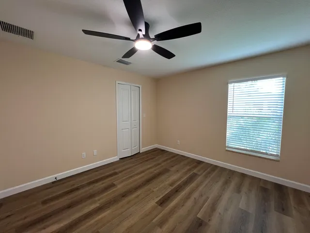 an empty room with wooden floor fan and windows