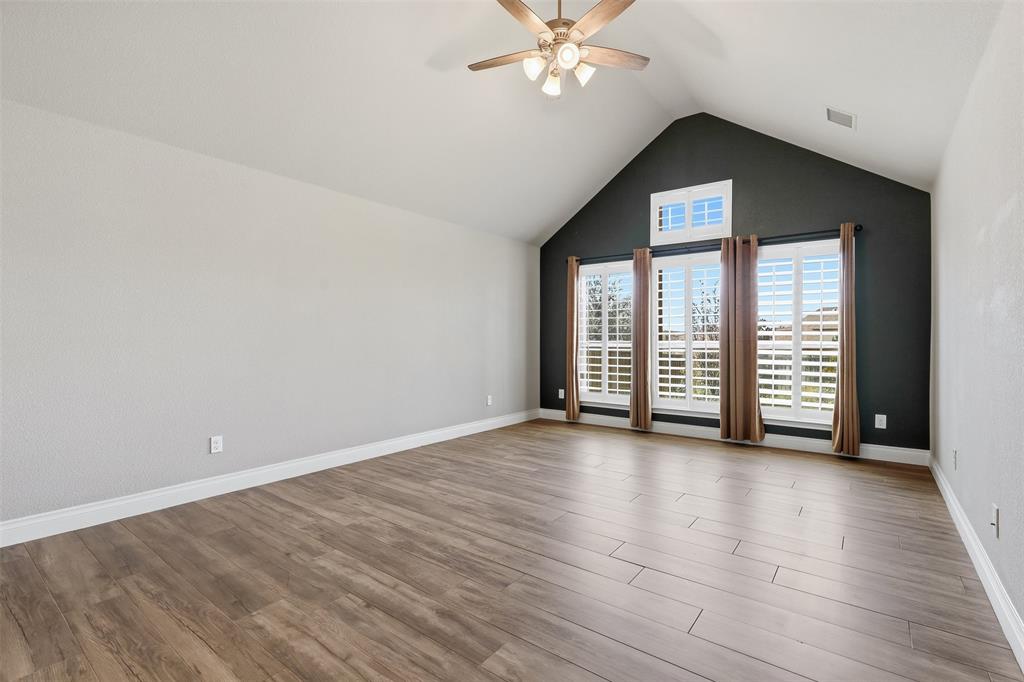 5640 Pradera Road Fort Worth, TX 76126 - Photo 16 of 35 Vaulted ceiling with a ceiling fan, wood-finish flooring, accent wall, and multiple windows with plantation shutters