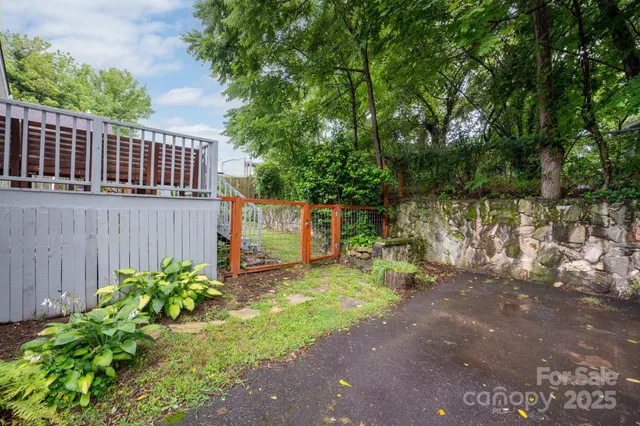 a view of a backyard with plants and large trees with wooden fence