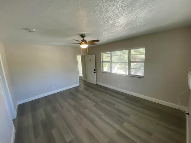 an empty room with wooden floor fan and windows
