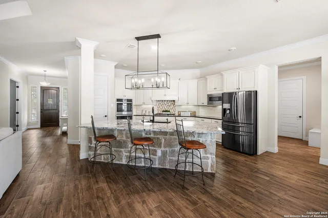 a kitchen with stainless steel appliances a refrigerator a stove a sink and chairs with wooden floor