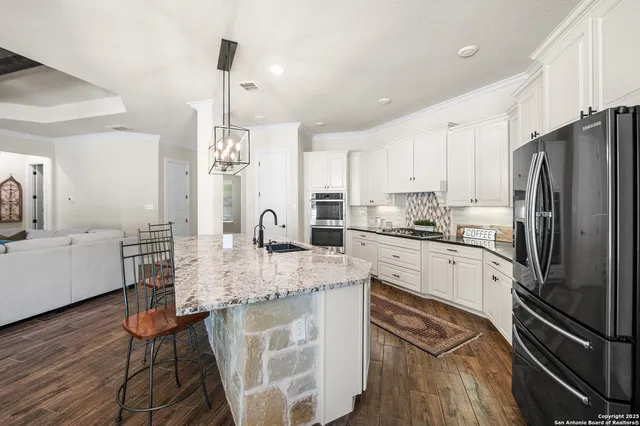 a kitchen with stainless steel appliances granite countertop a refrigerator a sink dishwasher a stove and white cabinets with wooden floor