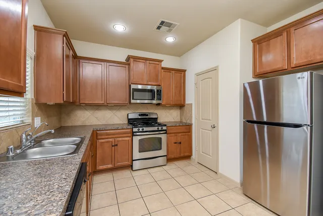 a kitchen with stainless steel appliances granite countertop a refrigerator a stove a sink a microwave and cabinets