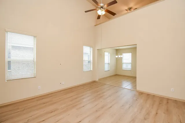 an empty room with wooden floor fan and windows