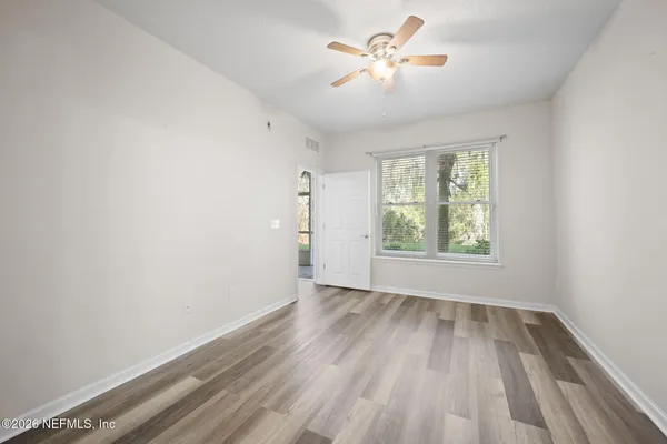 an empty room with wooden floor chandelier fan and windows