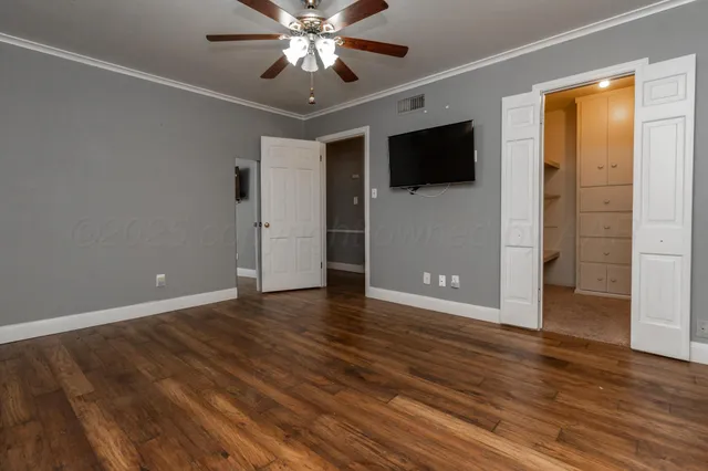 a view of an empty room with wooden floor and a ceiling fan