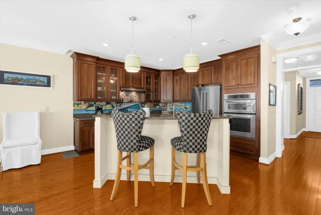 a kitchen with stainless steel appliances kitchen island granite countertop a refrigerator a stove a microwave oven a dining table and chairs with wooden floor