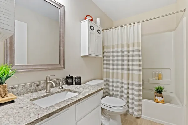 a bathroom with a granite countertop sink a toilet a mirror and shower curtain