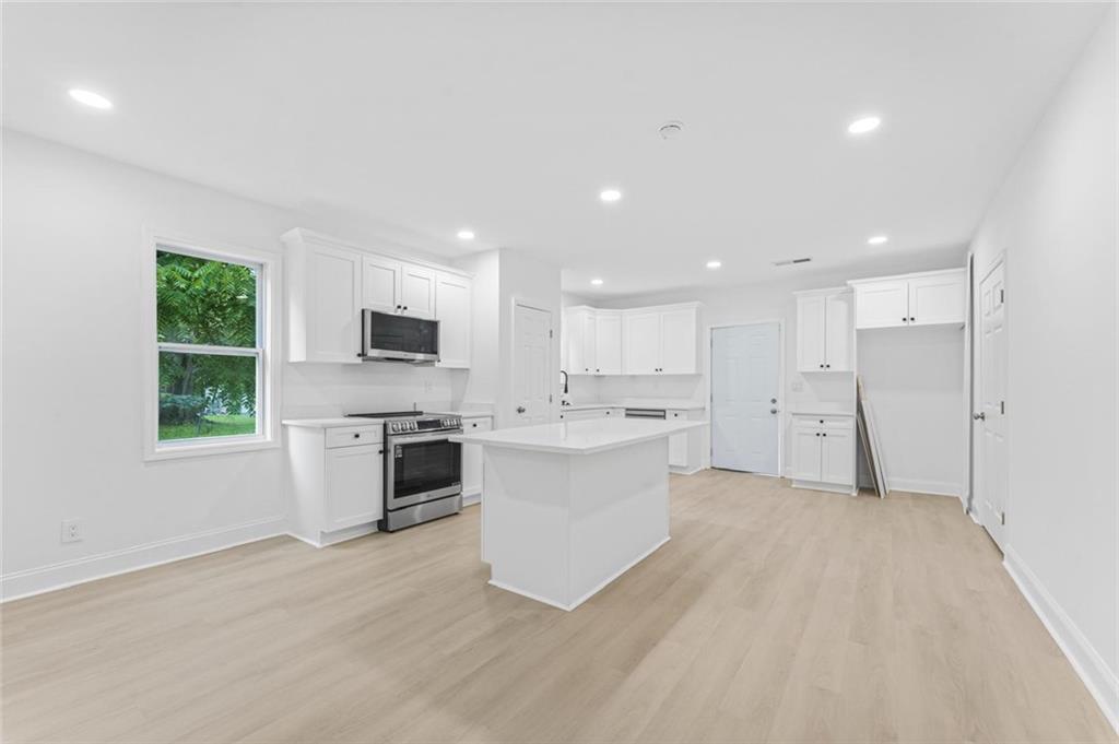 331 Highway 162 Covington, GA 30016 - Photo 9 of 26 a large white kitchen with stainless steel appliances granite countertop a stove a sink dishwasher and a refrigerator with wooden floor