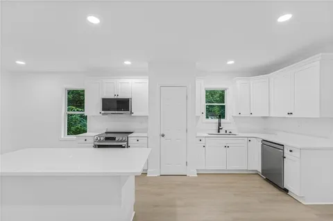 a large white kitchen with a sink a counter top space stainless steel appliances and a window