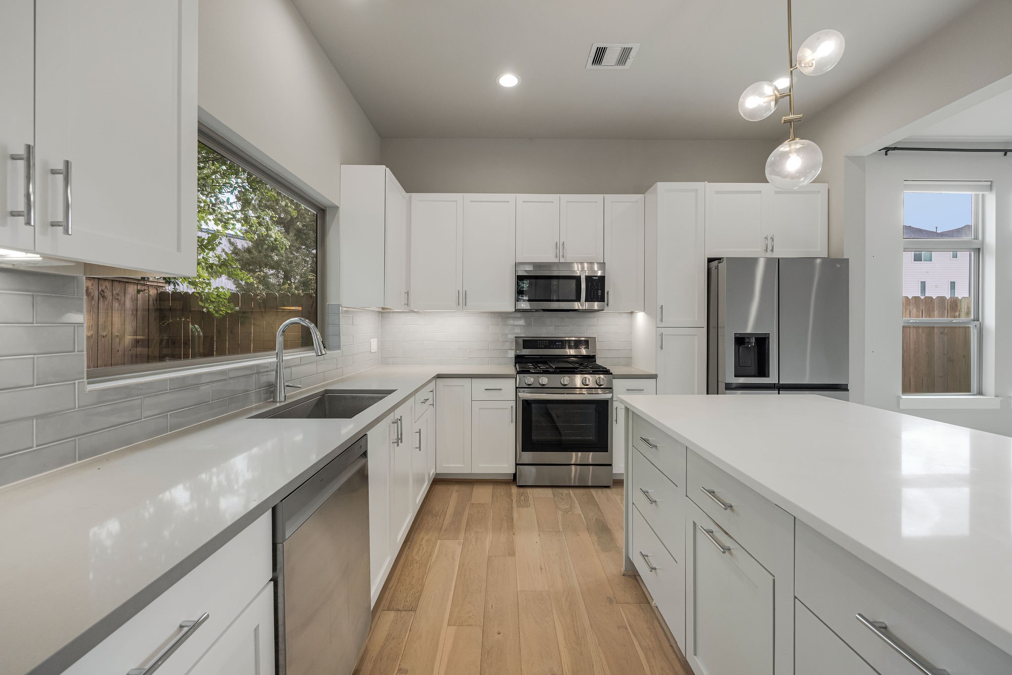 540 Janisch Road, Unit A Houston, TX 77018 - Photo 9 of 18 Sleek kitchen showcasing quartz countertops, white cabinetry, stainless steel appliances, subway tile backsplash, and a large center island with additional storage.