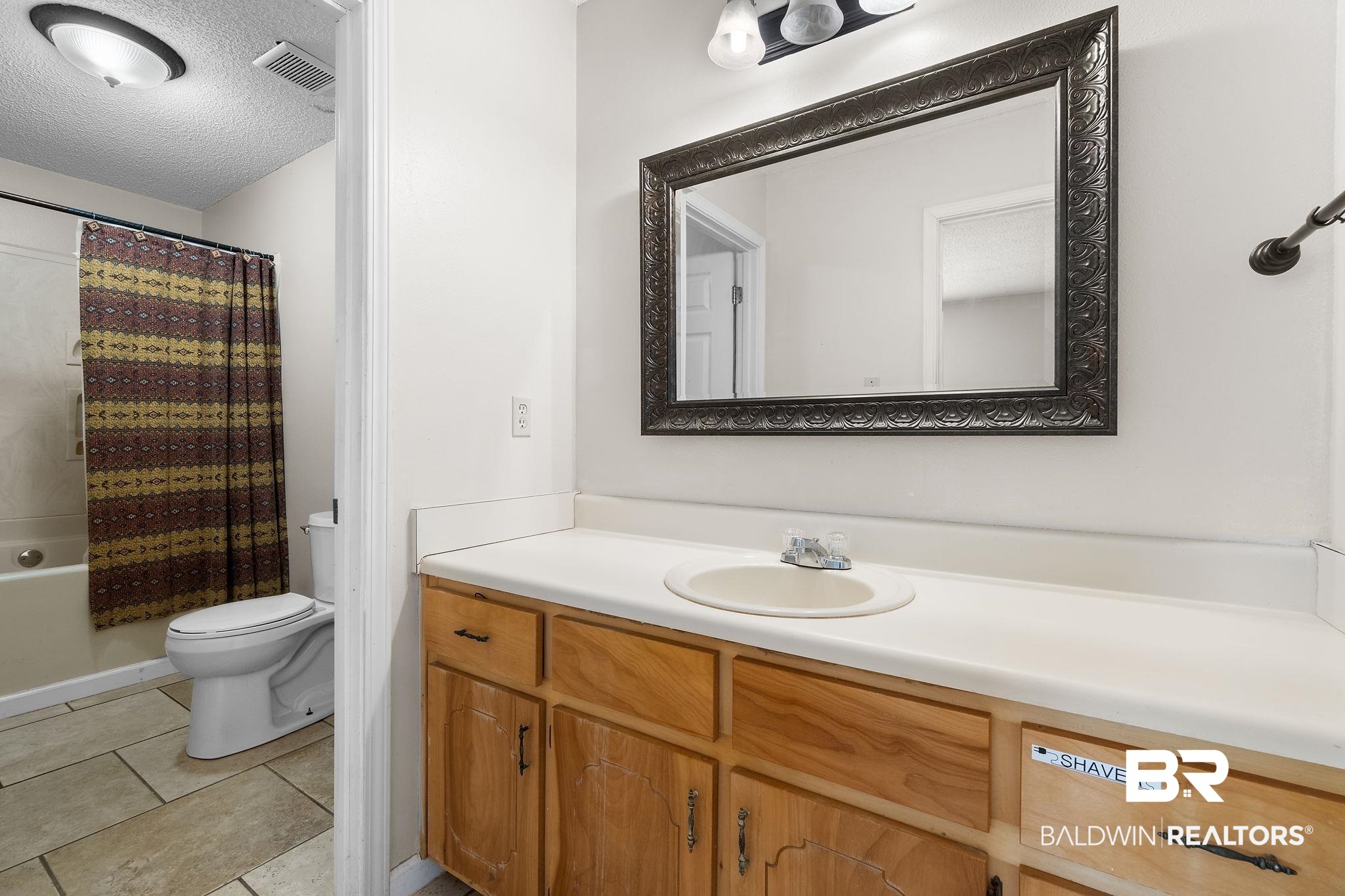 33135 Collier Road Lillian, AL 36549 - Photo 18 of 30 Bathroom with a textured ceiling, vanity, light tile patterned flooring, and shower / tub combo with curtain