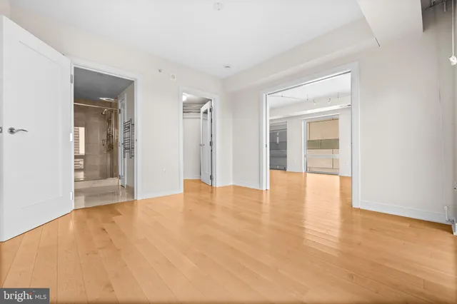 a view of an empty room with wooden floor and a kitchen