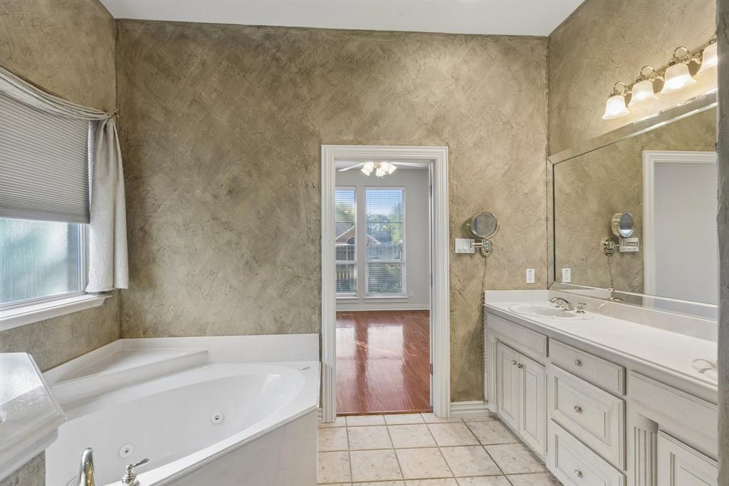 1727 Ridgecrest Drive Cleburne, TX 76033 - Photo 21 of 32 Dual vanity with white cabinetry, built-in jetted tub, tiled flooring, and a large wall-mounted mirror with integrated lighting