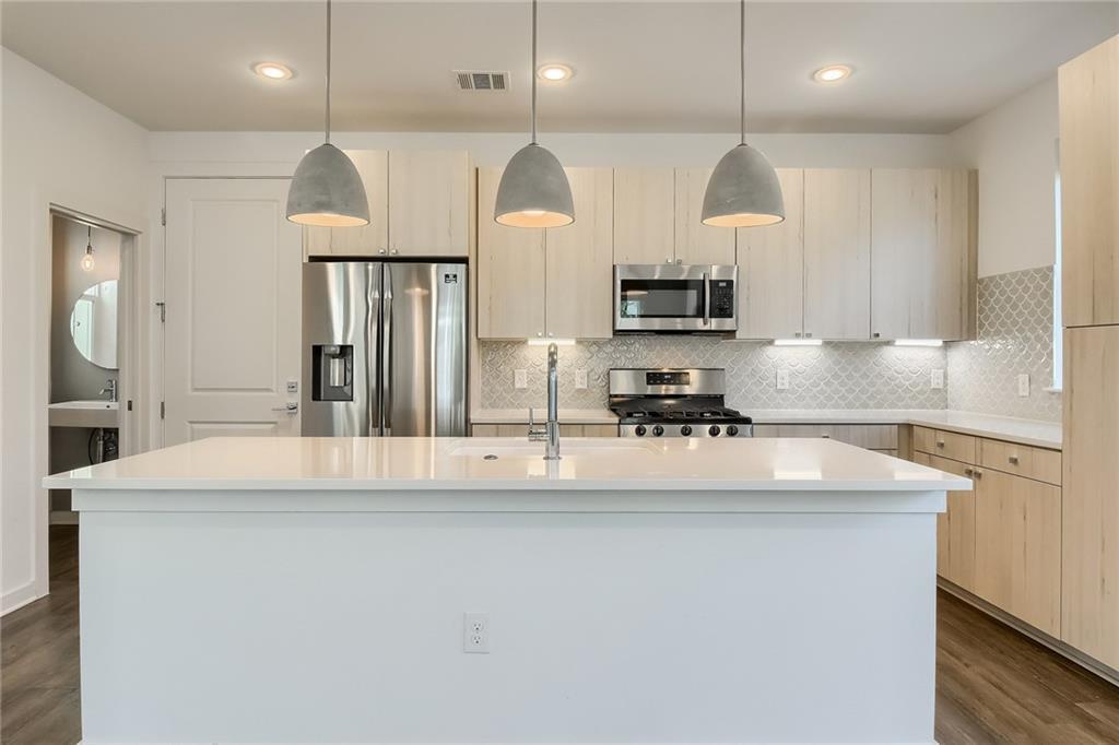 2624 Metcalfe Road, Unit 7 Austin, TX 78741 - Photo 10 of 31 Kitchen featuring a central island with a solid surface countertop, stainless steel appliances, wood-finish cabinetry, a decorative tile backsplash, and three pendant lights