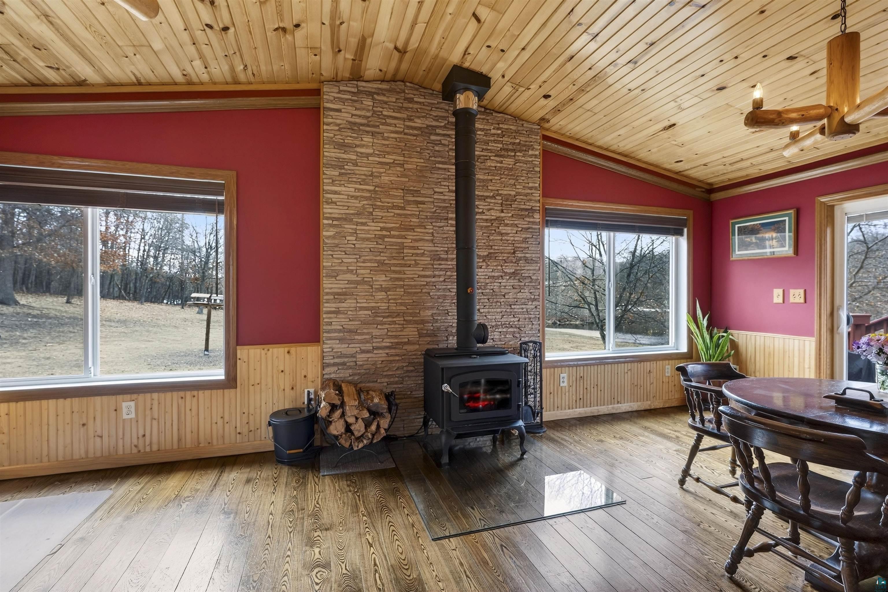 11702 East Mail Road Gordon, WI 54838 - Photo 32 of 49 Living area featuring wainscoting, light wood-style floors, a wood stove, plenty of natural light, and wood ceiling