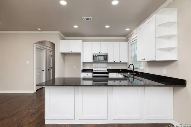 a kitchen with granite countertop white cabinets stainless steel appliances a sink and wooden floor