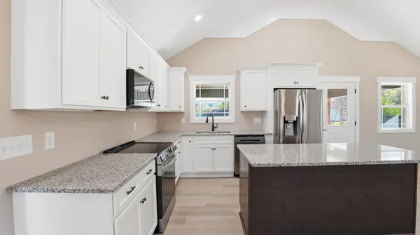 a kitchen with stainless steel appliances granite countertop a stove top oven a sink dishwasher and a refrigerator with wooden floor